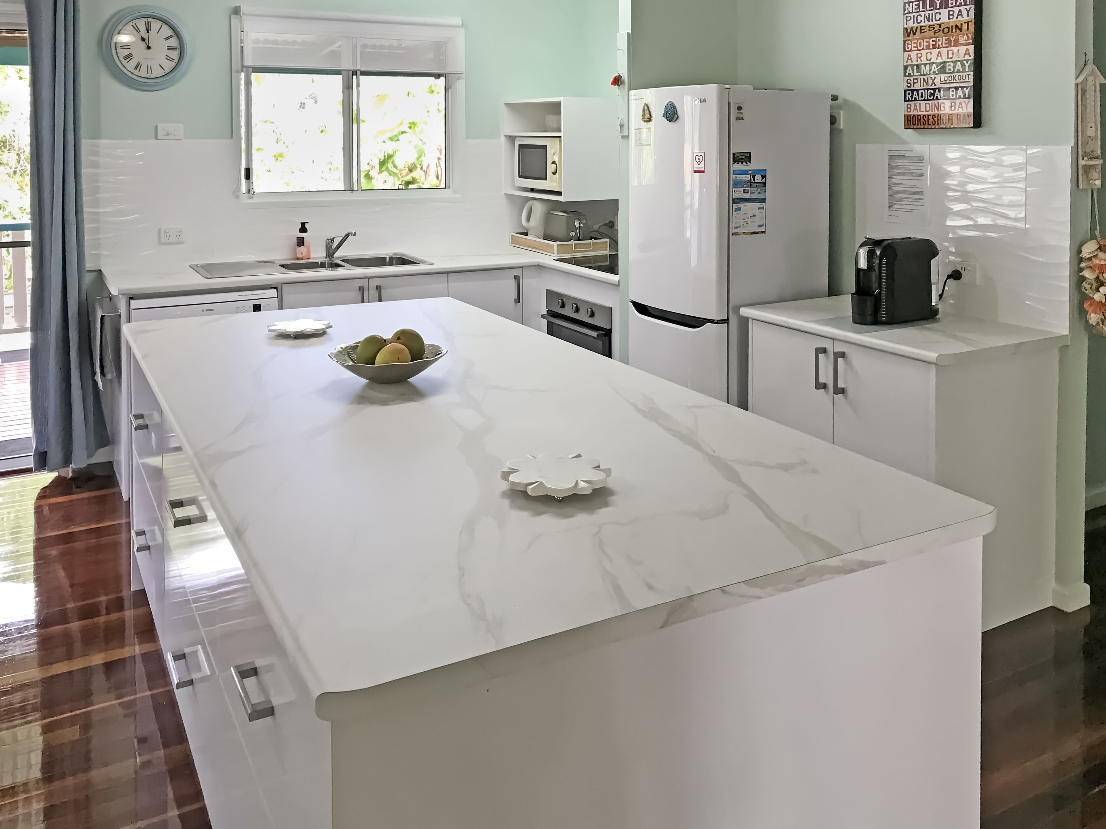Una cocina moderna con armarios blancos, encimera de mármol, fregadero, refrigerador y microondas.