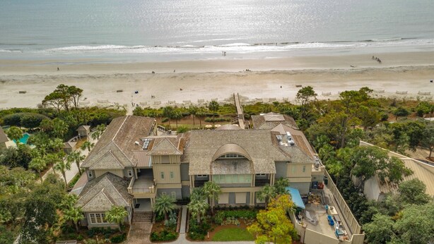 Una casa grande de dos pisos con piscina, rodeada de exuberante vegetación y vista a la playa.