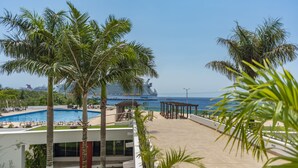 Zona de piscina en un resort, con palmeras, un pabellón y vista al océano y un crucero.