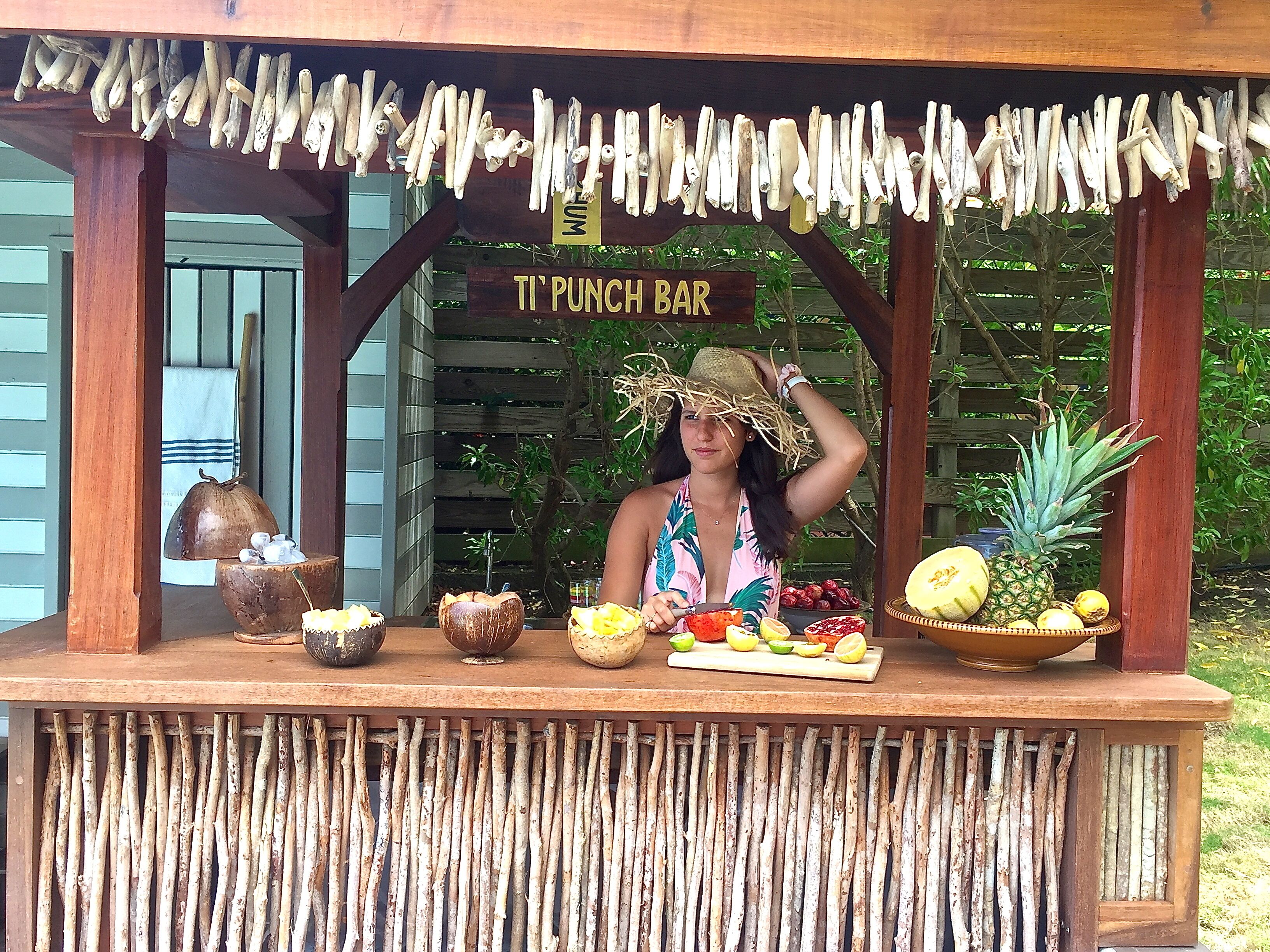 A tropical-themed bar named "Ti Punch Bar" with a wooden structure, a sign, and various fruits displayed on the counter.