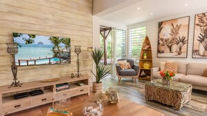 A modern living room with a large TV displaying a beach scene, a wooden TV stand, a sofa, a coffee table, and a bookshelf. - La Sirène du Diamant ,18 guests
Spacious beachfront rental in Martinique : (LE DIAMANT)