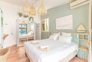 Une chambre à coucher avec un lit, des tables de chevet, un miroir, une grande fenêtre et une vue sur la mer.