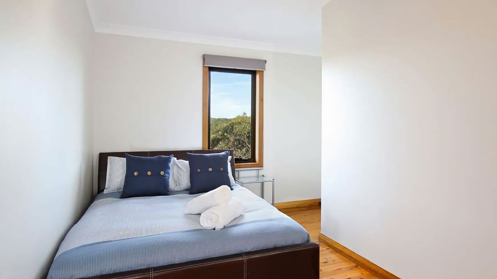 A bedroom with a bed, pillows, a window, and a view of greenery.