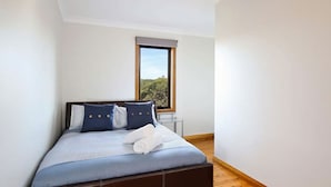 A bedroom with a bed, pillows, a window, and a view of greenery. - Postcards From The Edge (Blackheath)