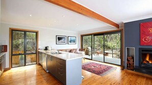 A modern kitchen with a central island, large sliding glass doors to a patio, and a fireplace. - Postcards From The Edge (Blackheath)