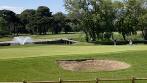 Een golfbaan met een waterhindernis, een bunker en een vlag.