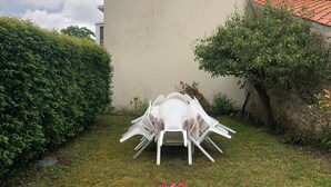 A garden with a white plastic table and chairs, a hedge, and a building with a tiled roof. - old house in the heart of sallertaine, garden, shopping on foot (Sallertaine)
