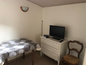 Ein schlichter, einfach eingerichteter Raum mit einem Bett, einem Schminktisch, einem Stuhl und einem Fernseher.