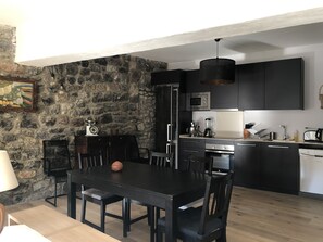 Une cuisine moderne avec des meubles de couleur sombre, un mur en pierre et un coin repas comprenant une table et des chaises en bois.