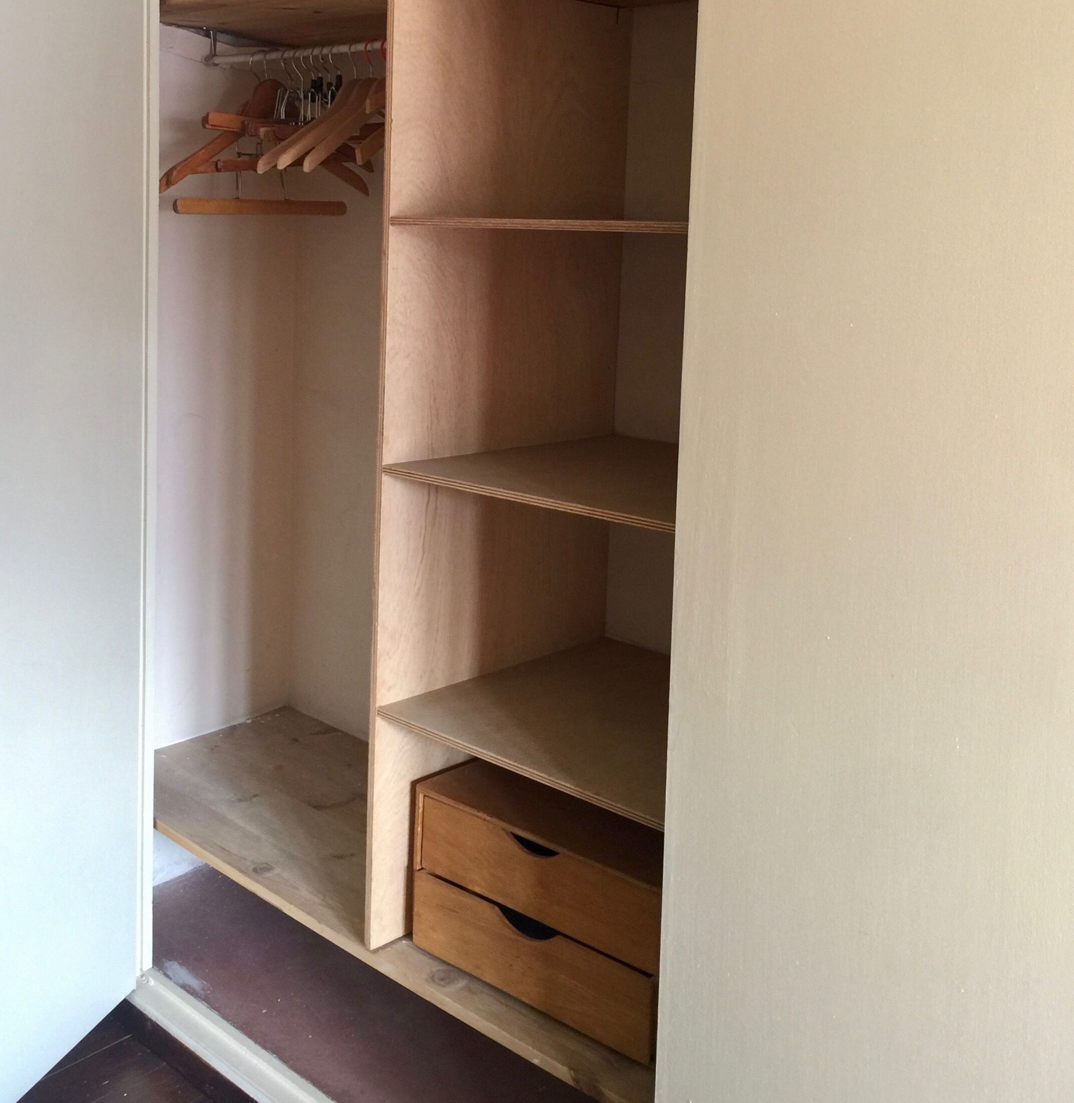 A wooden wardrobe with multiple shelves and a lower drawer.