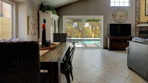 Amplia sala de estar con comedor, chimenea, televisor y vista a una piscina.