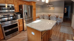 A kitchen with wooden cabinets, stainless steel appliances, a granite countertop island, and pendant lighting. - Amazing in ground Pool, 5 bedroom 3 bath, Short Walk to Town and  Beach (South Haven)