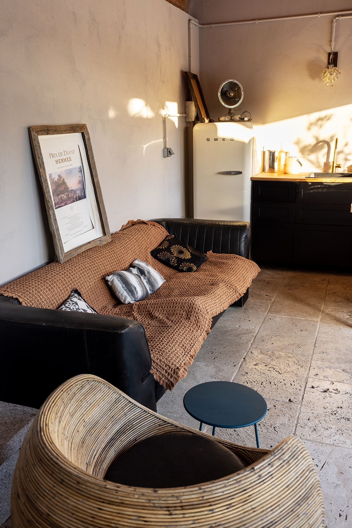 Une pièce confortable comprenant un lit, une petite table ronde, un fauteuil en osier et un coin cuisine.