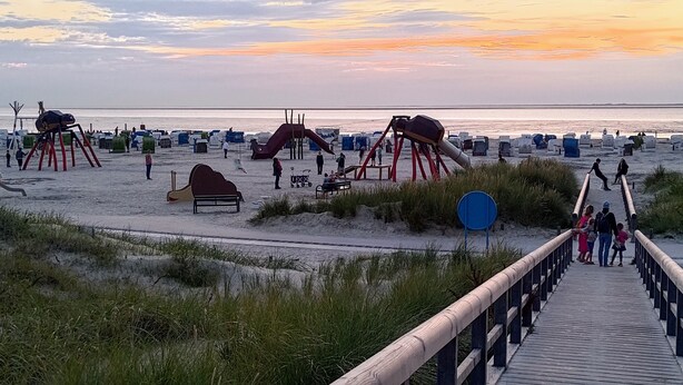 A beach with a wooden boardwalk leading to beach chairs and umbrellas.
