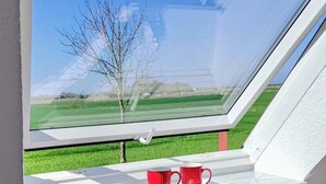 A room with a skylight, two red stools, and a view of a green field and tree.