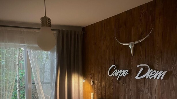 Un dormitorio con cama, pared de madera, ventana con cortinas, mesita de noche y lámpara de pared.