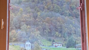 A room with a large window overlooking a mountainous landscape with autumn foliage and a small building in the distance. - Cauterets : 6 person chalet - 65 m2 5 mn from town center, 30 mn from Lourdes  (Cauterets)