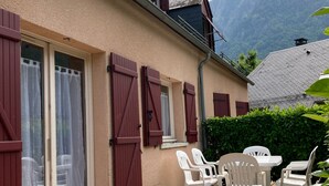 A building with a tiled patio, red shutters, and a table with chairs. - Cauterets : 6 person chalet - 65 m2 5 mn from town center, 30 mn from Lourdes  (Cauterets)