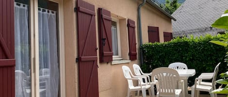 A building with a tiled patio, red shutters, and a table with chairs.
