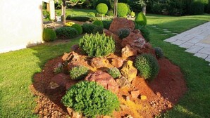 Ein angelegter Garten mit einem Felsen im Mittelpunkt, ordentlich geschnittenen Hecken und einer Pergola.