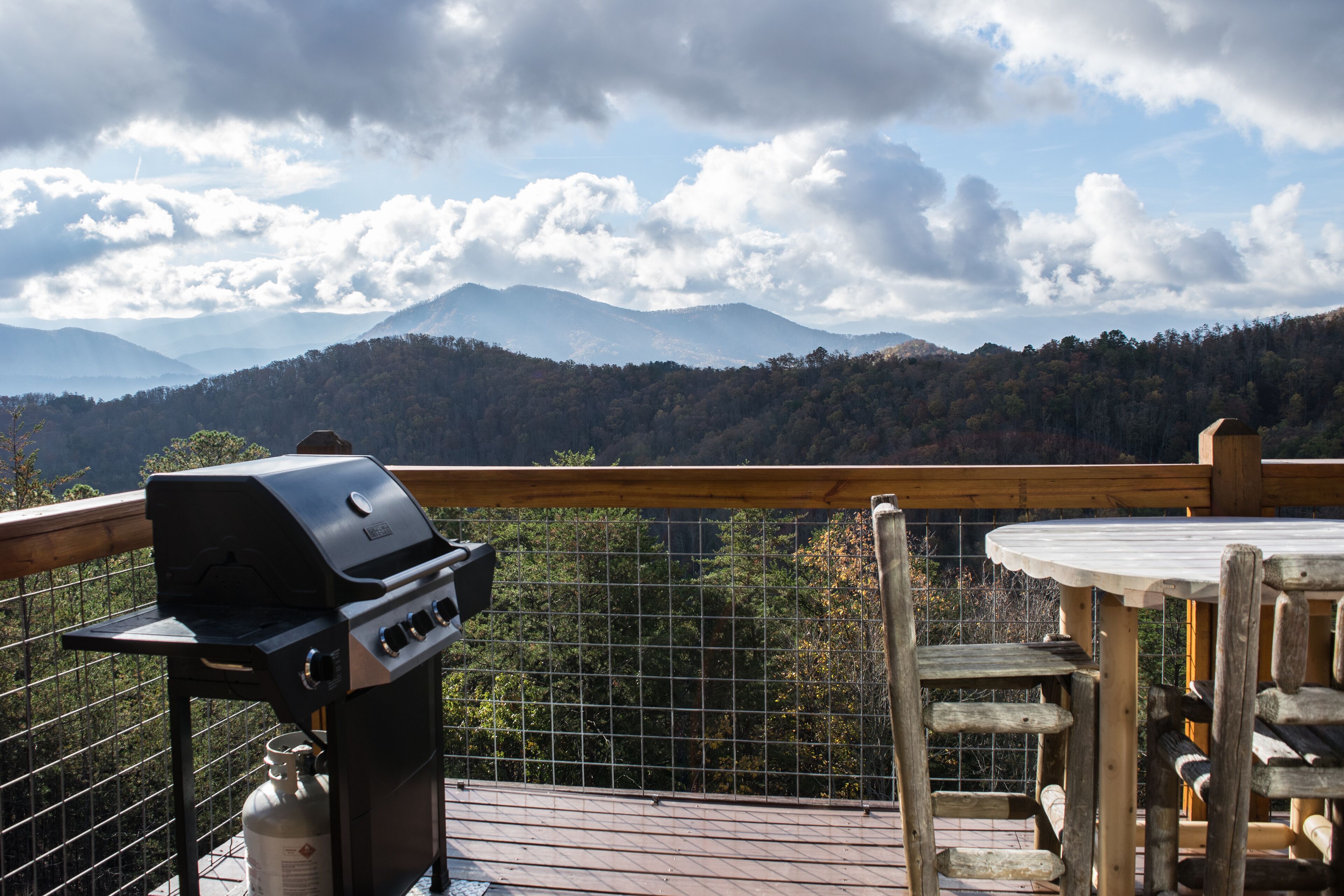 A balcony with a grill, wooden table, and chairs.