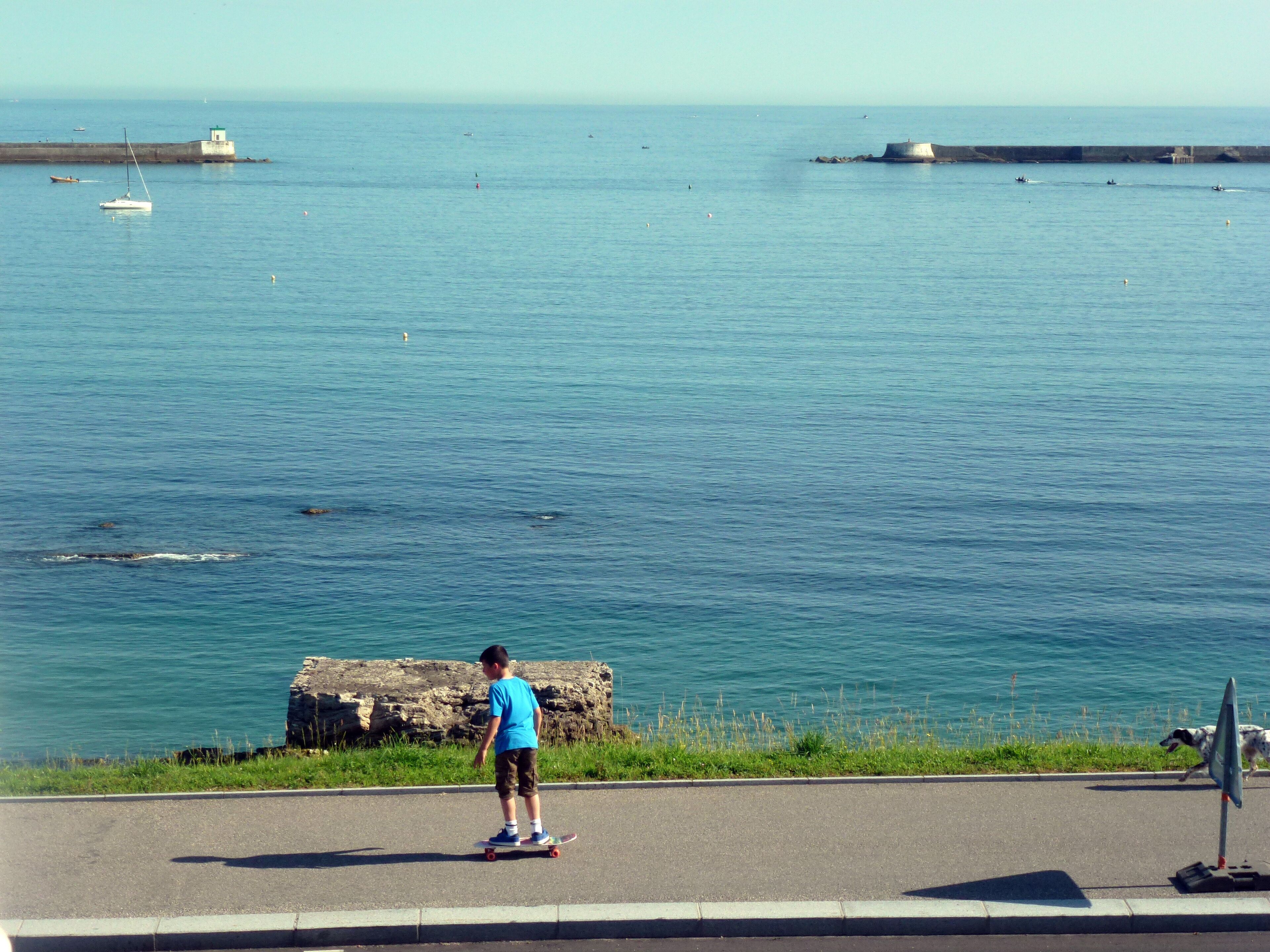 A coastal road with a clear view of the sea and a lighthouse in the distance.