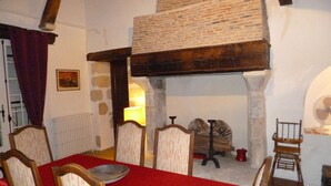 Een eetruimte met een rode tafelkleed, houten stoelen, een bakstenen openhaard en een stenen muur.