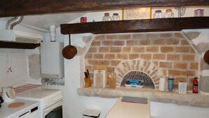 Een keuken met een open haard van baksteen, witte apparaten en een houten tafel.