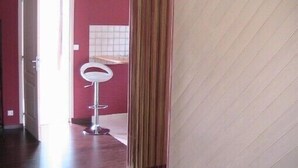 A room with a wooden floor, a white chair, and a door leading to another room. - Charming quiet apartment in Villa with garden (Cambo-Les-Bains)