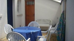 A small patio with a table and chairs, a wooden door, and a white wall. - Charming quiet apartment in Villa with garden (Cambo-Les-Bains)