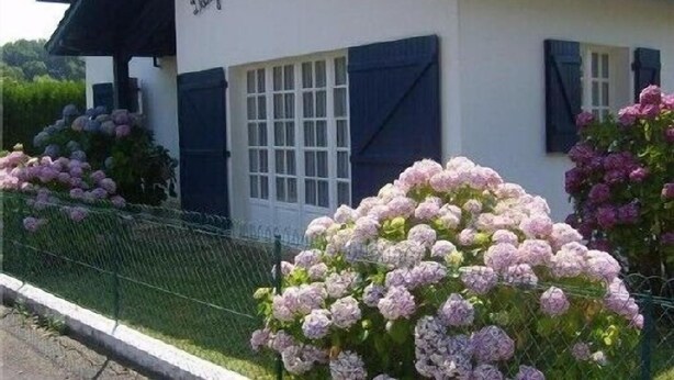 A building with a white facade and dark shutters, surrounded by a metal fence. - Charming quiet apartment in Villa with garden (Cambo-Les-Bains)