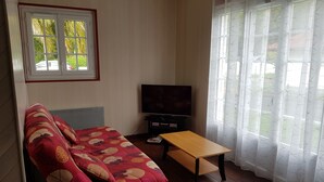 A living room with a sofa, a TV, a coffee table, and a window with curtains. - Charming quiet apartment in Villa with garden (Cambo-Les-Bains)