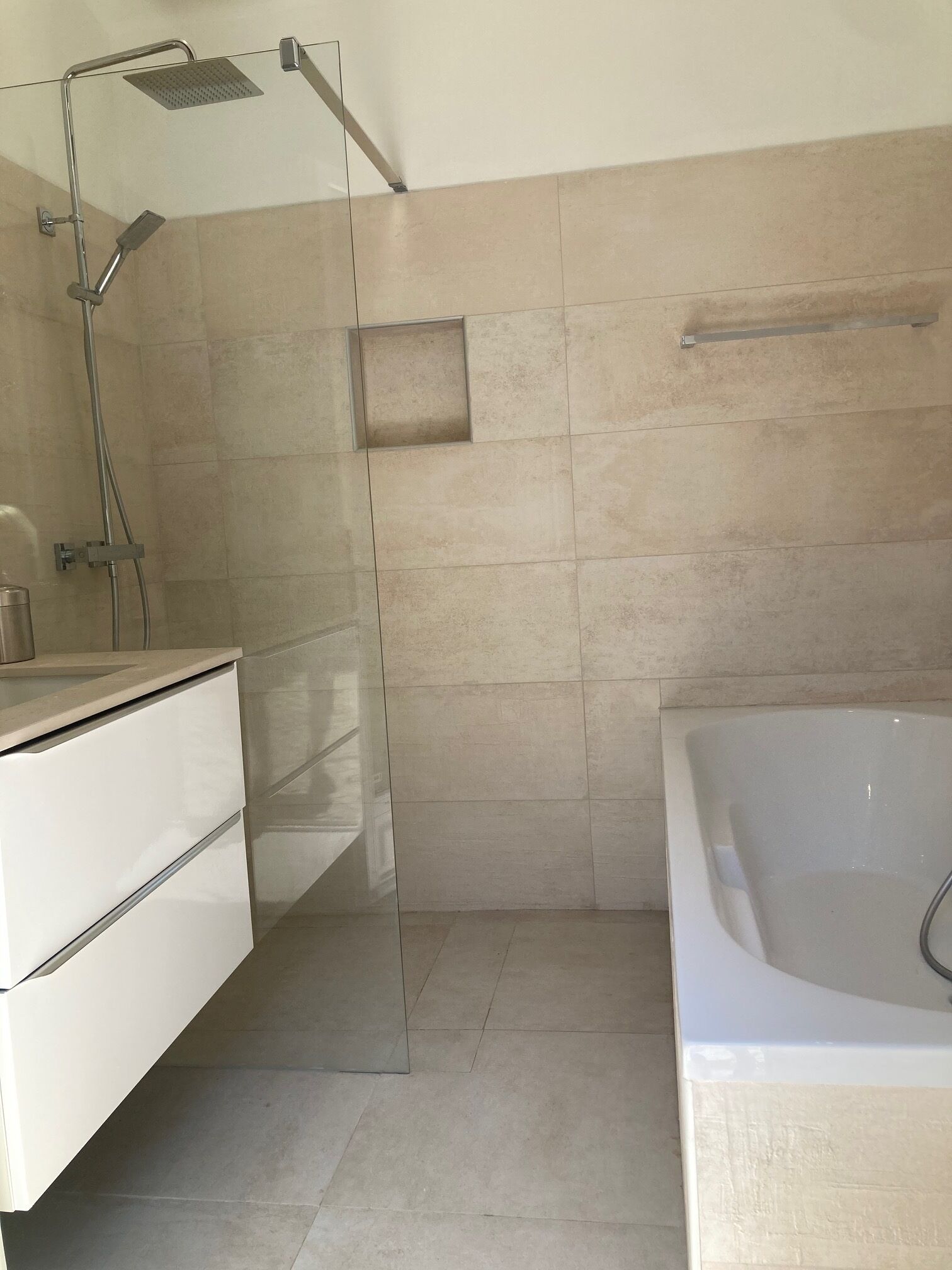 A modern bathroom with a glass shower enclosure, a white bathtub, and a minimalist vanity.