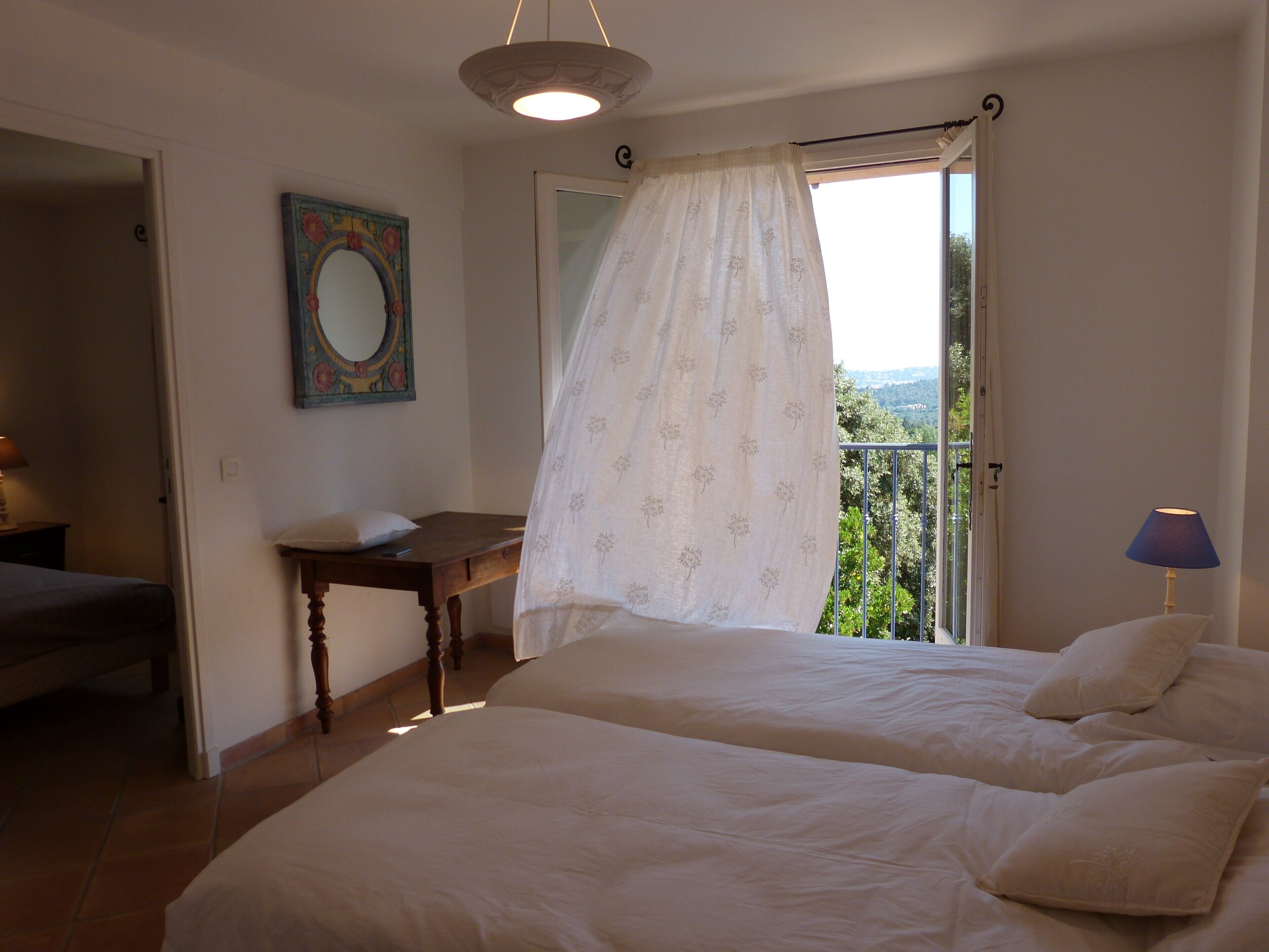 Ein Schlafzimmer mit zwei Betten, einem Nachttisch, einem Spiegel und Blick ins Freie.
