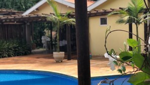 Una piscina con un porche de madera y un edificio amarillo al fondo.