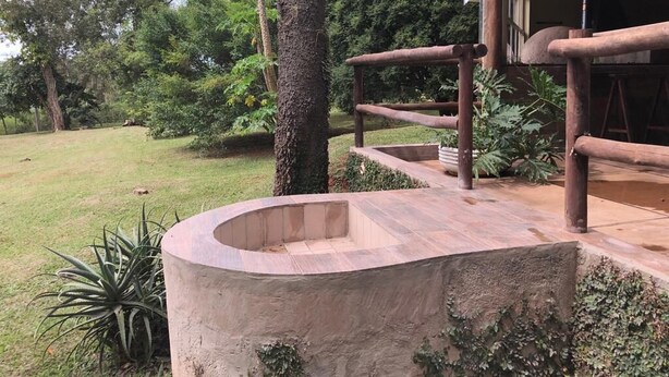 Un banco de piedra en un jardín con valla de madera y un edificio al fondo.