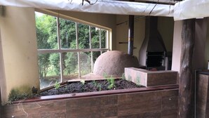Un espacio al aire libre rústico con un amplio ventanal, un horno de piedra y un banco de madera.