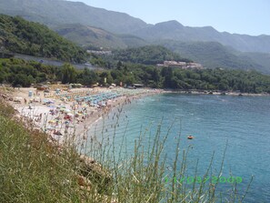 Una playa con sombrillas y gente, rodeada de montañas.