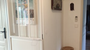 Ein Flur mit einer weißen Tür, einem kleinen Holzschemel, einem an der Wand montierten Telefon und einer Lampe auf einem Beistelltisch.