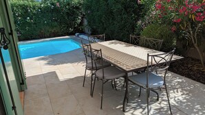 Eine Außenpatio mit Pool, Tisch und Stühlen, umgeben von viel Grün.
