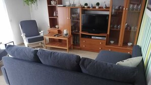 Una sala de estar con un sofá azul oscuro, un mueble de madera para entretenimiento con un televisor y una mesita con un control remoto.
