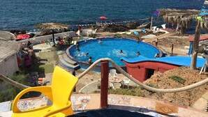 Zona de piscina con vista al océano, rodeada de sillas de playa y sombrillas.