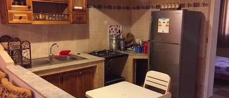A compact kitchen with a gas stove, sink, and a refrigerator. There is a dining table with chairs.