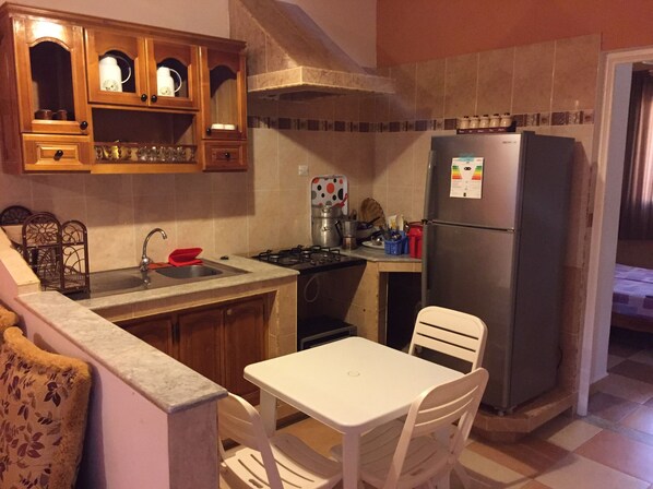 Une cuisine compacte équipée d’une cuisinière à gaz, d’un évier et d’un réfrigérateur. On y trouve également une table à manger avec des chaises.