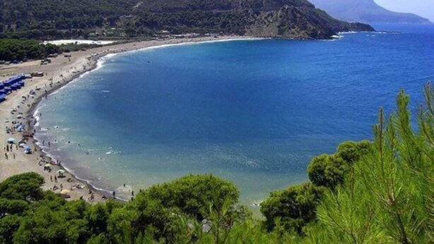 Una playa costera con vistas despejadas al océano y un telón de fondo montañoso.