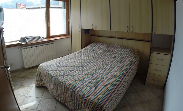 Una camera da letto con un letto, una finestra, un termosifone e pensili in legno.