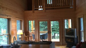 A cabin with a wooden interior, a dining area with a sink, a sofa, a TV, and a balcony with a railing. - Gorgeous Rustic Northern Michigan Island Getaway (St. James)