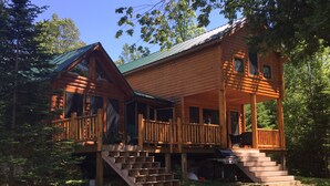 A log cabin with a porch, outdoor seating, and a dog. - Gorgeous Rustic Northern Michigan Island Getaway (St. James)