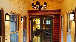 A wooden interior with a central door, flanked by windows with lights, and a chandelier above. - Gorgeous Rustic Northern Michigan Island Getaway (St. James)