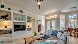 Uma sala de estar moderna com um amplo sofá modular, uma TV de tela plana e estantes embutidas com objetos decorativos.